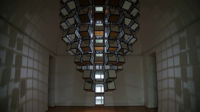 Pouring light via grid panes creating shifting shadows, suspended cube artwork rotating in gallery