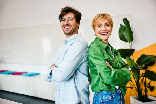 Cheerful businessman and businesswoman cross arms in the office