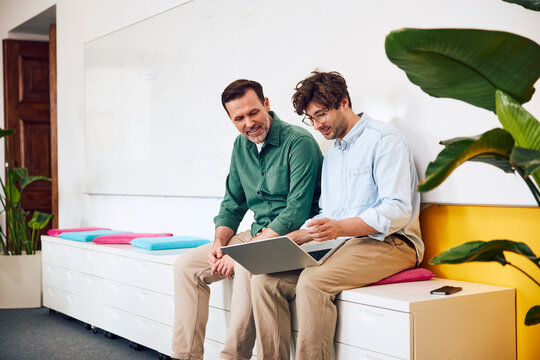 Male colleagues discuss work on a laptop in a casual office