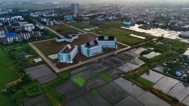 Aerial view of modern office buildings surrounded by agricultural rice paddies and urban development in the Gedebage area of Bandung, West Java, Indonesia.