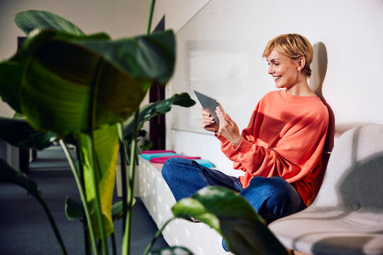 Cheerful businesswoman using tablet while relaxing in office