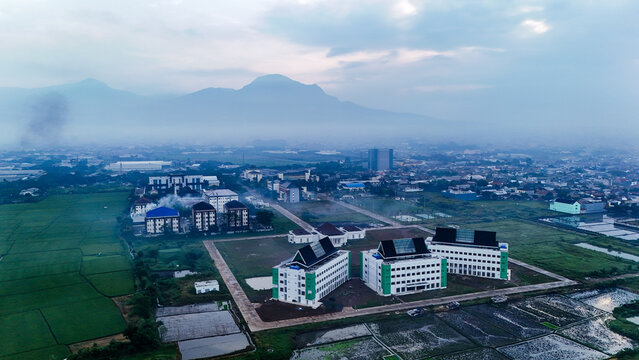 Aerial view of the Gedebage area featuring modern buildings surrounded by green rice fields and agricultural land in Bandung, West Java, Indonesia.
