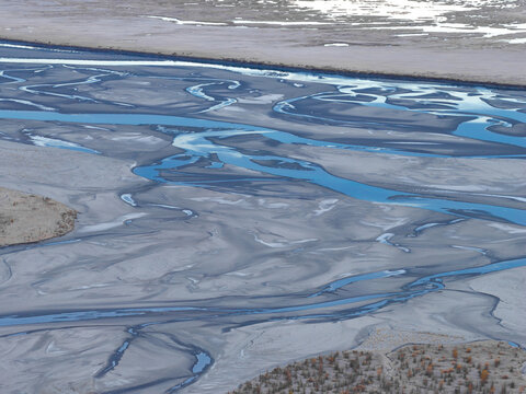 Aerial view of the braided Knik River with its intricate blue water channels, glacial silt deposits, and sandbars winding through the landscape in Knik River, Alaska, United States.