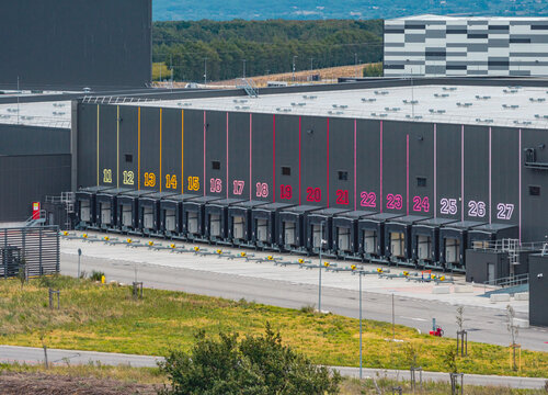 Aerial view of a modern logistics warehouse featuring a long row of numbered loading docks, empty truck bays, and large industrial distribution infrastructure in France.
