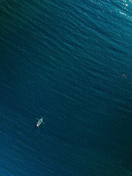 Single white kayak paddling through deep blue ocean waves under clear sunlight reflections in...