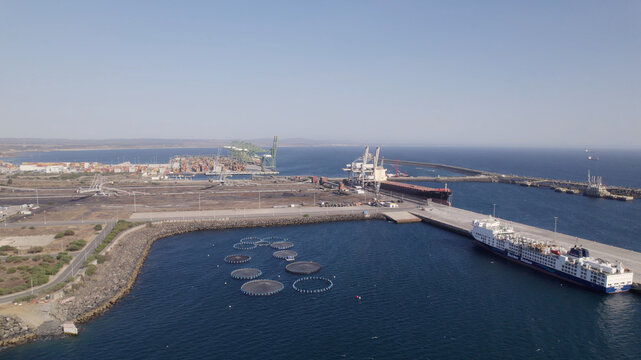 Aerial view of the Port of Sines featuring industrial infrastructure, cargo ships, and fish farming cages in the Atlantic Ocean, Sines, Setubal, Portugal.