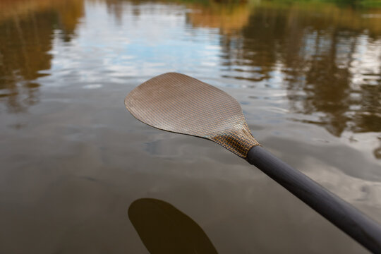 Single kayak paddle blade held above water surface with river bank reflections
