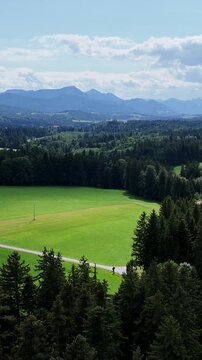 Picturesque landscape of Bavaria with view of Alps and green forests. Bird's eye view of bright green meadow, dense coniferous forest and majestic mountain ranges on the horizon. Tourism, nature