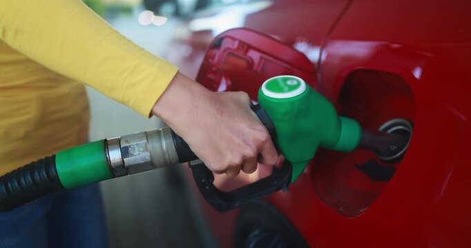Close up of woman hand pumping gasoline fuel in car at gas station - Inflation, transport and rising fuel prices concept - Focus on hand - UGC content
