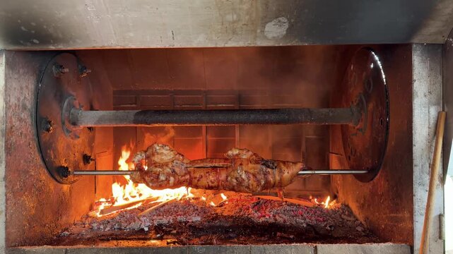 Whole Pig Roasting on a Rotisserie Spit over an Open Wood Fire in a Rustic Steel Pit: Traditional Barbecue in Motion. Roasting a Whole Pig for a Feast