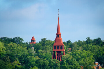 Blick auf einen roten, historischen Glockenturm, der von Wald umrahmt ist in Stockholm, Schweden am 04.September 2025 © joerghartmannphoto