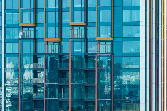 Aerial view of luxury residential apartments featuring a modern glass facade with balconies and geometric orange accents in Warszawa, Mazowieckie, Poland.
