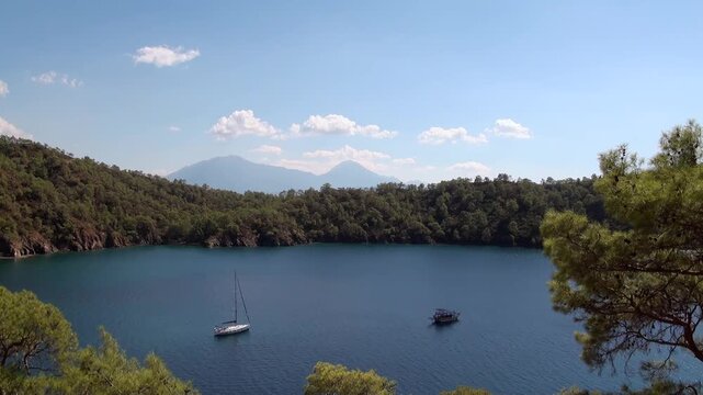 Boats on Calm Water With Layered Wooded Hills Beyond. The scene combines blue water, rocky slopes and pine vegetation from a natural elevated coastal viewpoint.
