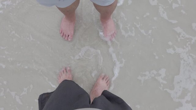 view looking down on ground while 2 asian mans walking on the white sand beach with sea and wave in Samed Island of Thailand.walks barefoot on the beach and leaves footprints in the sand