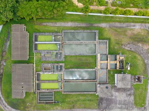 Aerial view of a water treatment plant with rectangular filtration tanks, green algae-covered basins, and concrete infrastructure surrounded by grass in Karangan, Kedah, Malaysia.