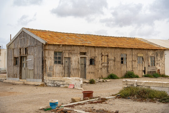 Old, neglected wooden house standing under a cloudy sky, showing signs of decay and abandonment in a rural or coastal landscape, evoking themes of desolation and forgotten places