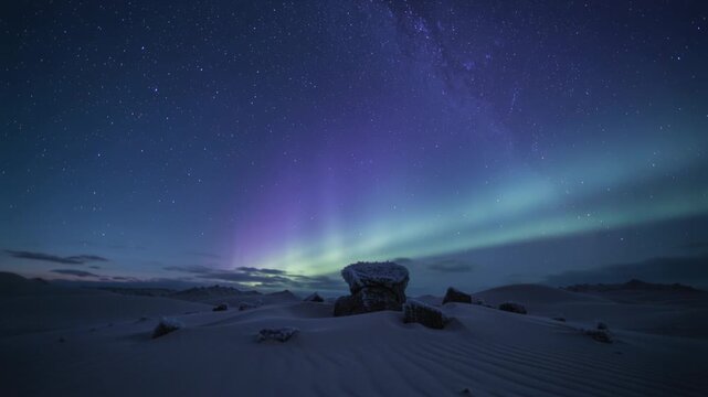 Blooming aurora forming purple curtains over dunes with storm, lighting center boulder and stars