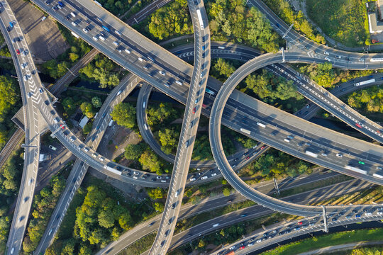 Aerial view of a complex highway interchange with multiple levels of roads and flowing traffic surrounded by lush green trees in the United Kingdom.