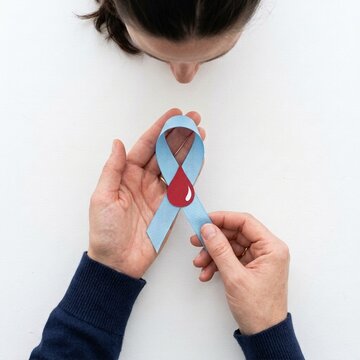 Hands holding blue awareness ribbon with red blood drop symbol for diabetes and health awareness