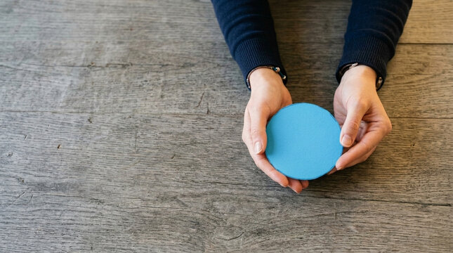 Hands Holding Blue Circle Object on Wooden Surface