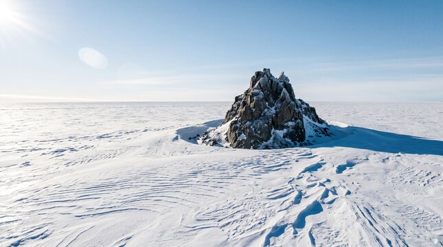 Solitary rugged granite peak rising from snowfields across an endless polar ice sheet under bright harsh sunlight for wilderness endurance and polar climate concept