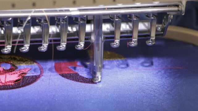Embroidery Needles Stitching a Red Design on Blue Fabric. The footage documents textile equipment, material handling, stitching or machine controls in a workshop.