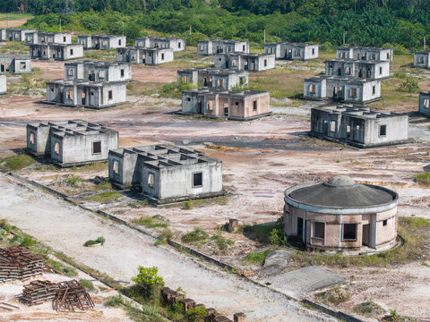 Aerial view of an abandoned housing project with unfinished concrete structures and a circular building in a rural landscape in Karangan, Kedah, Malaysia.