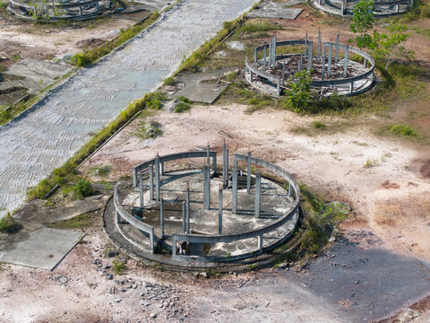 Aerial view of circular concrete foundations of an abandoned building project set in a desolate landscape with dirt ground and sparse vegetation in Karangan, Kedah, Malaysia.
