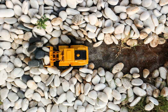 Top view of a yellow toy bulldozer moving white and black pebbles to create a path, representing construction and heavy equipment.