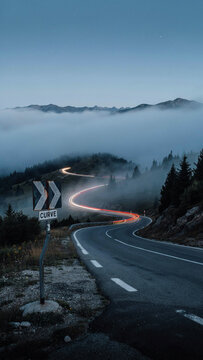 Winding mountain road with vehicle light trails at dusk under fog mountain landscape transport highland adventure direction traveling atmospheric twilight