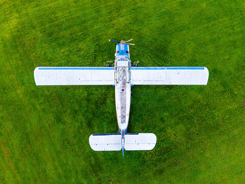 Aerial view of a small propeller plane parked on a vibrant green grass field in Latvia.