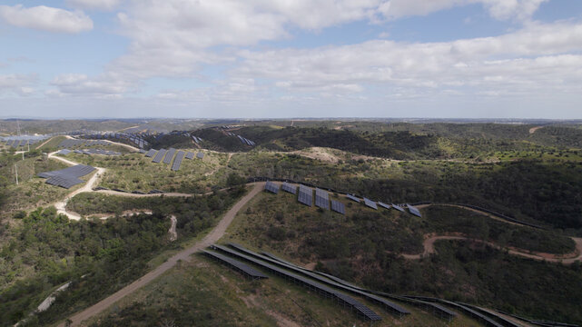Aerial view of the Morgado de Arge Photovoltaic plant with rows of solar panels installed on rolling hills under a blue sky with scattered clouds in Portimao, Faro, Portugal.