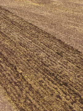 Aerial view of a freshly plowed agricultural field with distinct soil textures and parallel furrows in Latvia.