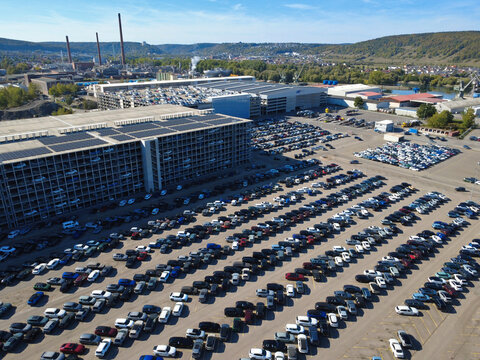 Aerial view of the car terminal in Kelheim, featuring rows of parked vehicles, large multi-level parking structures with solar panels, and industrial facilities in Kelheim, Bavaria, Germany.