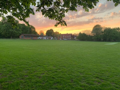 Colourful sunset over a village playing field framed by leaves
