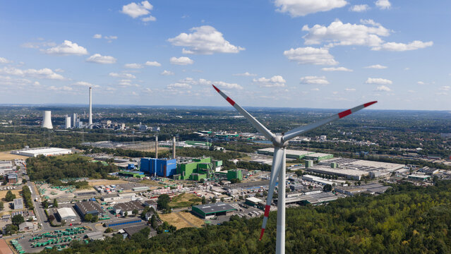 Aerial view of a wind turbine at Halde Hoppenbruch with an industrial landscape and power plant in the background under a blue sky in Herten, North Rhine-Westphalia, Germany.