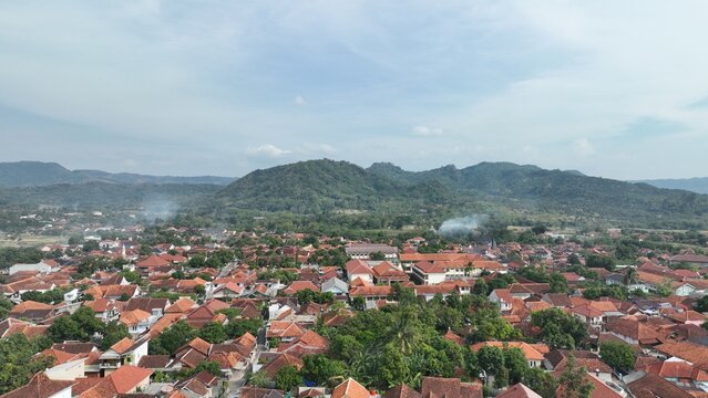 Aerial view of the town of Majalengka with terracotta rooftops, lush green trees, and distant mountains under a clear sky in Majalengka, West Java, Indonesia.