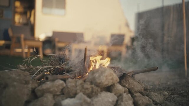 Small campfire burning on rocks outdoors with a camper van and outdoor furniture in the background