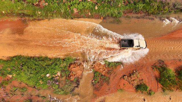 Aerial view of a 4x4 utility vehicle driving through a flooded rural dirt road in Louis Trichardt, Limpopo, South Africa.