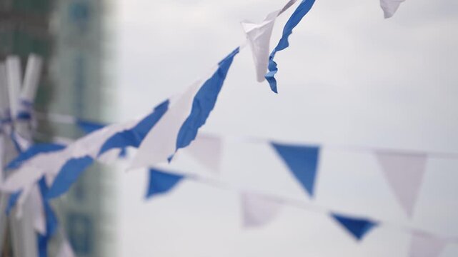 cinematic shot of blue and white triangular pennant flags string bunting fluttering in the wind against a bright sky at an outdoor festival or event