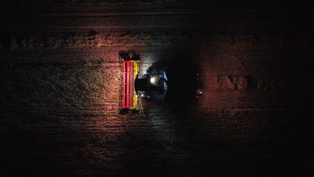 Aerial view of a combine harvester working in a field at night, illuminated by its own lights in Crepaja, Vojvodina, Serbia.