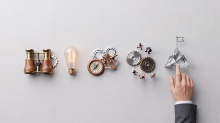 Fototapeta premium Top down overhead view of business strategy concept with binoculars, light bulb, compass, gears, and a hand pointing at a crystal mountain peak with a flag representing success and goals
