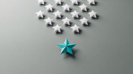 Fototapeta premium Conceptual Overhead Shot of a Unique Teal Blue Paper Origami Star Leading a Group of White Stars on a Grey Background, Representing Leadership, Individuality, Success, and Standing Out.
