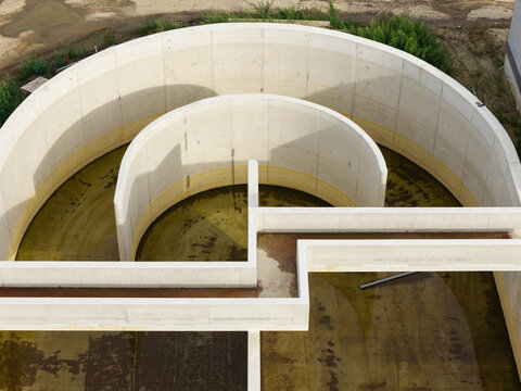 Aerial view of a circular concrete wastewater treatment basin with industrial infrastructure and water management systems in Diepenbeek, Flanders, Belgium.
