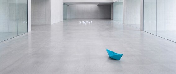 Fototapeta premium A single blue origami paper boat standing out from a group of white boats in a large minimalist modern architectural hall with concrete floors, representing leadership and individuality.