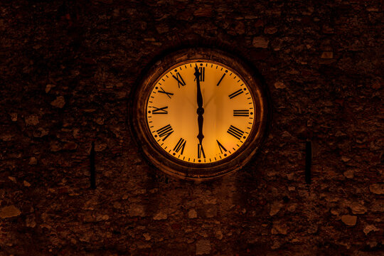 wall outrood clock on the old yellow stone tower of a night town or city showing 6