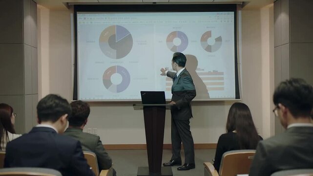 Checking laptop, presenter in suit pointing to pie chart on screen in meeting room explaining data