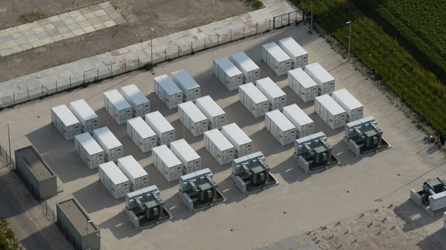 Aerial view of a battery energy storage system with rows of white shipping containers and electrical transformers in a fenced industrial site in Dronten, Flevoland, Netherlands.