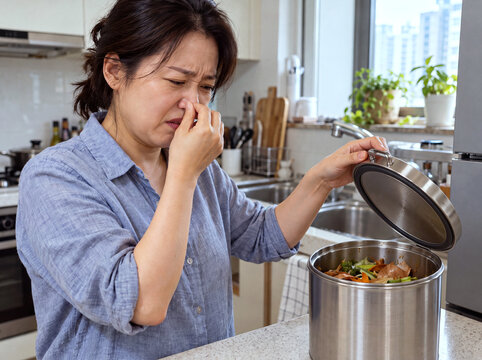 Woman pinching her nose while opening a food waste bin