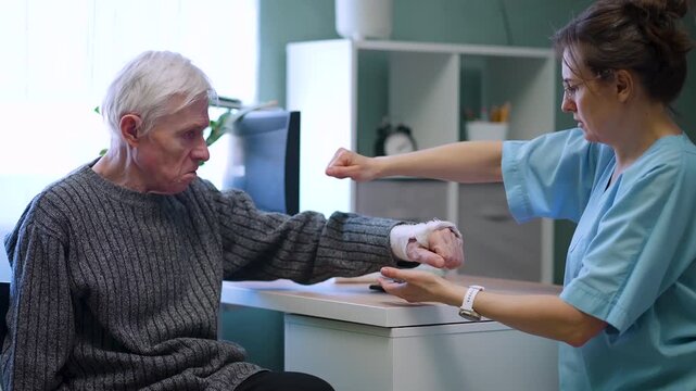 Caring nurse reaches out to test reflexes and finger mobility in elderly patient recovering from fracture. Medical professional gently assesses joint movement to ensure proper rehabilitation progress
